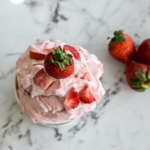A bowl of homemade strawberry ice cream with fresh strawberries on a marble countertop.