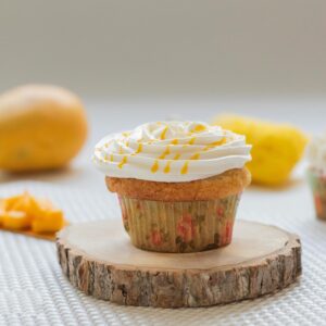 Close-up of a mango cupcake with cream frosting, surrounded by fresh mango pieces.