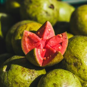 A pile of ripe green guavas with a vibrant pink sliced guava on top, highlighting freshness.