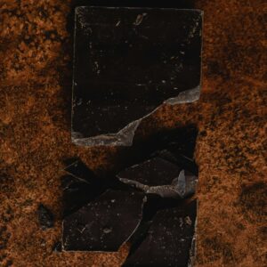 Close-up of broken dark chocolate on a textured brown surface. Ideal for dessert themes.