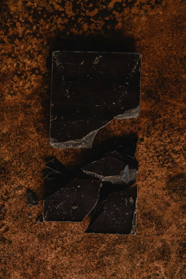 Close-up of broken dark chocolate on a textured brown surface. Ideal for dessert themes.